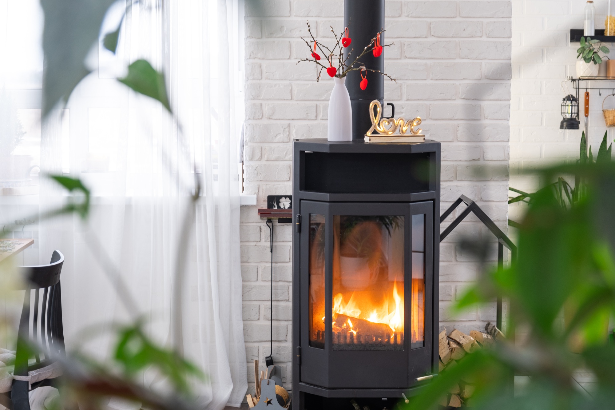 Valentine decor near fireplace stove with fire and firewood. Cozy home hearth