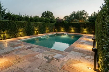Éclairage extérieur autour d'une piscine moderne avec bornes et spots encastrés sur terrasse en pierre naturelle au crépuscule