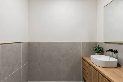 Salle de bain moderne avec carrelage céramique grand format et dalle murale effet plâtre, séparés par un profilé laiton, avec vasque blanche et meuble en bois